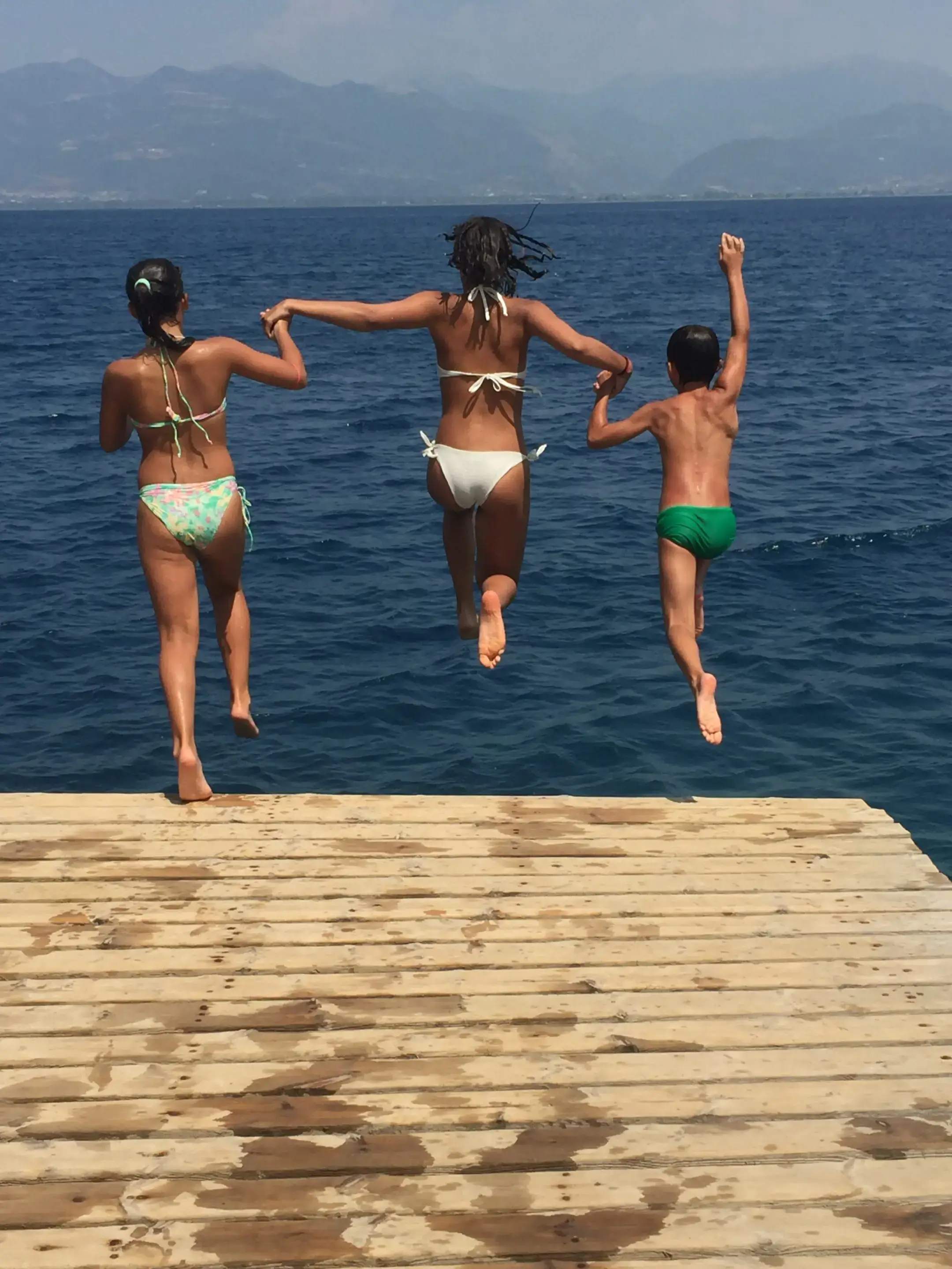 Three people jumping off a pier into the ocean.